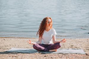 A woman meditating on a beach during a sunny day.